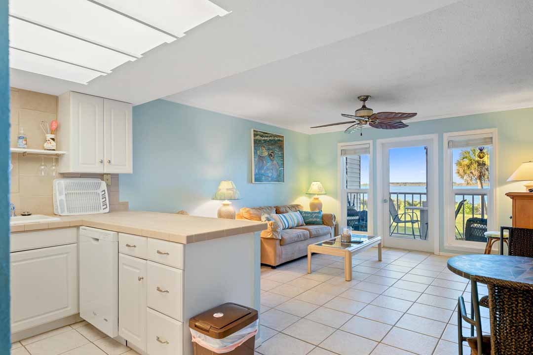 Brightly lit beachfront apartment interior with an open kitchen, living area, and balcony doors overlooking the sea.