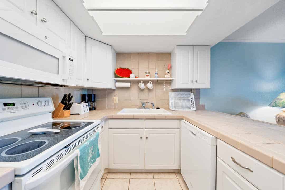 A neat, modern kitchen with white cabinetry, beige countertops, built-in appliances, and decorative items on shelves.