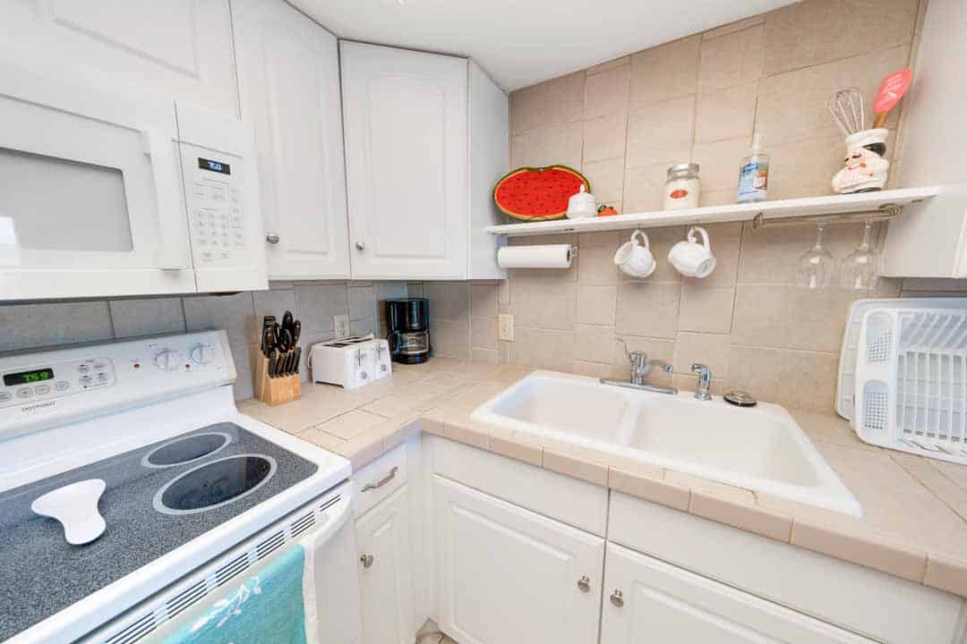 Compact kitchen featuring white appliances, wooden cabinets, and a tiled backsplash, with a red pot holder hanging on the wall.