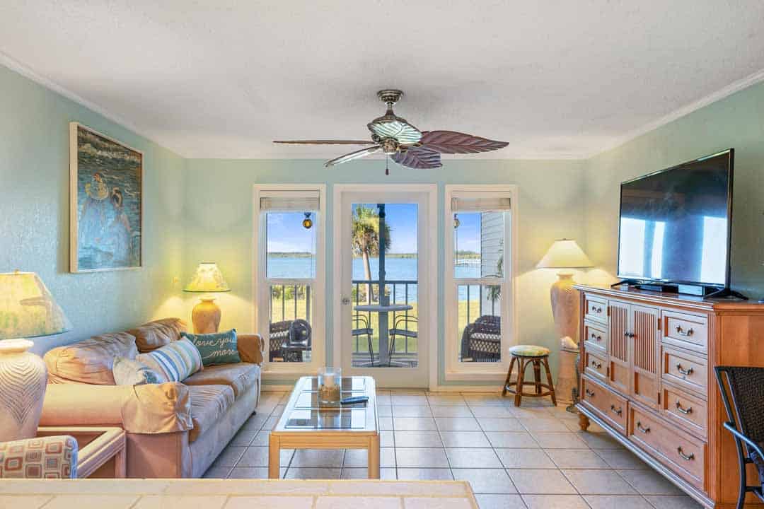 A beachfront living room with soft blue walls, a couch, a tv, and sliding doors leading to a balcony with ocean views.