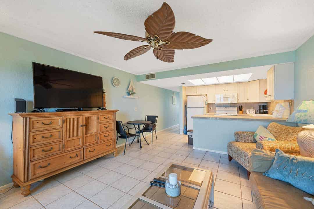 Interior of a cozy living room featuring a tv, sofa, dining area, and an open kitchen with light blue walls and a tile floor.