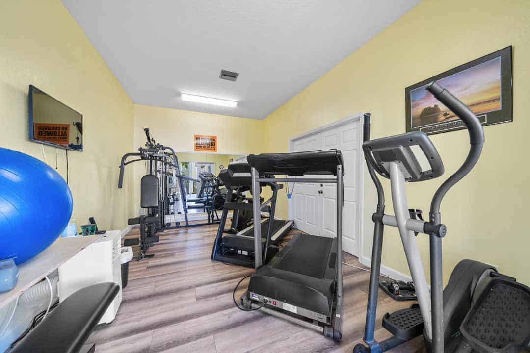 Home gym room with various exercise equipment including a treadmill, elliptical, and weight machine, with bright yellow walls and framed pictures.