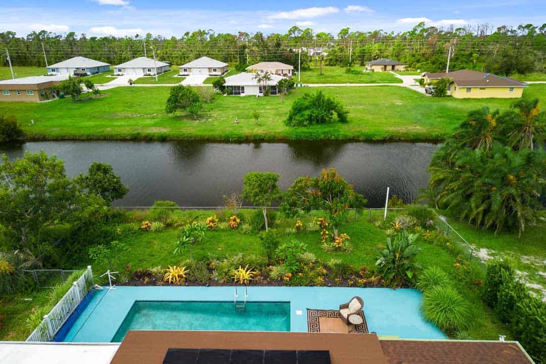 Aerial view of a backyard with a large swimming pool in Rotonda, overlooking a small lake and surrounded by multiple residential houses.