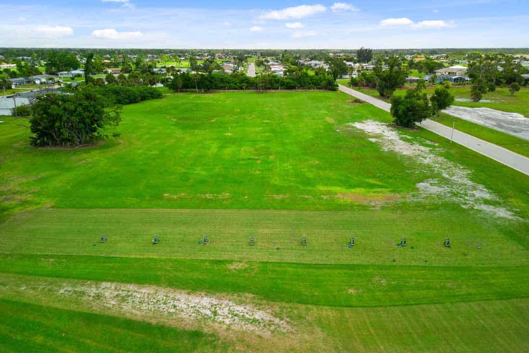 Aerial view of a lush green park with a row of evenly spaced trees in Rotonda, surrounded by a residential area under a cloudy sky.