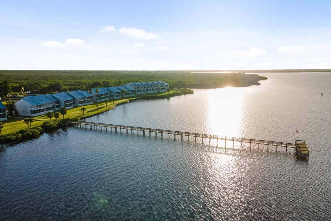 Aerial view of waterfront buildings with a long pier extending into a calm lake, illuminated by sunlight.