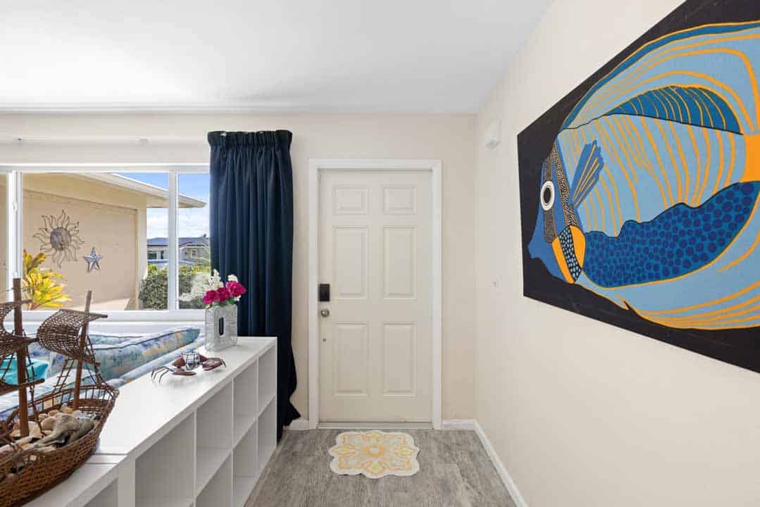 A modern entryway featuring a large blue and yellow fish painting on the wall, a white door, and a small Rotonda console table with decorative items.