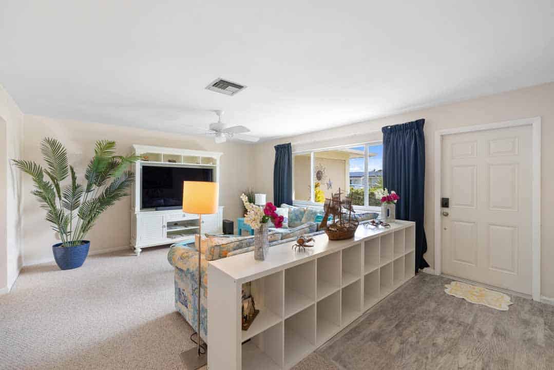 Bright, cozy living room with a floral sofa, white entertainment unit, decorative plants, and blue Rotonda curtains.