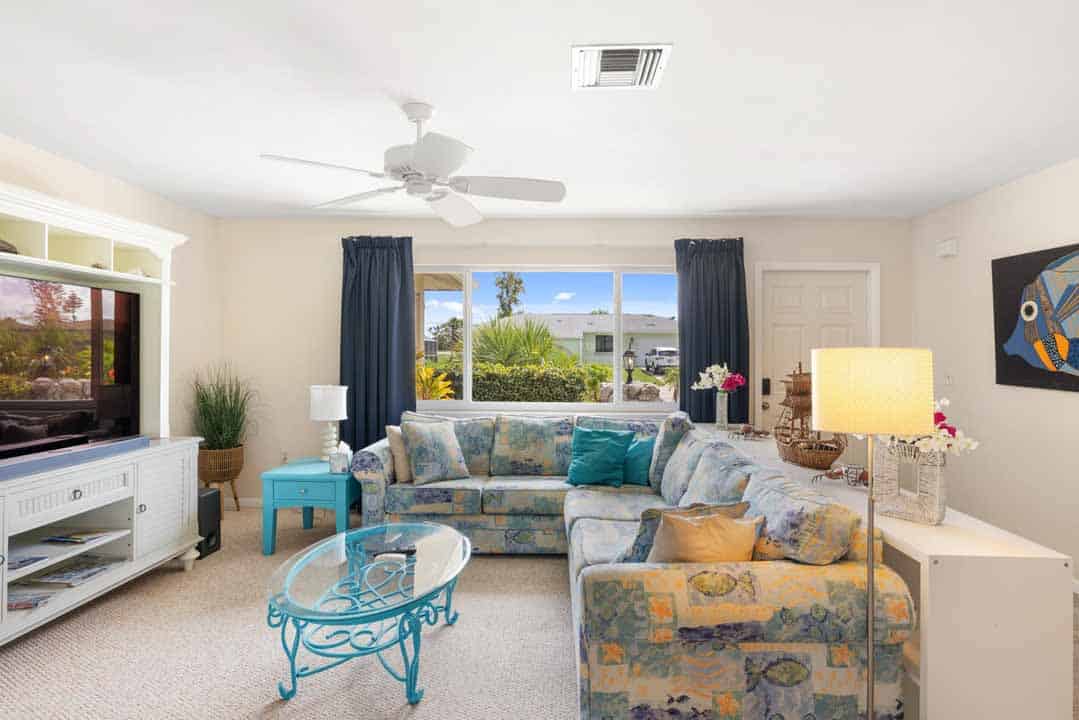 Bright living room with floral sofa set, a turquoise coffee table, and a view of a sunny landscape through large rotonda windows.