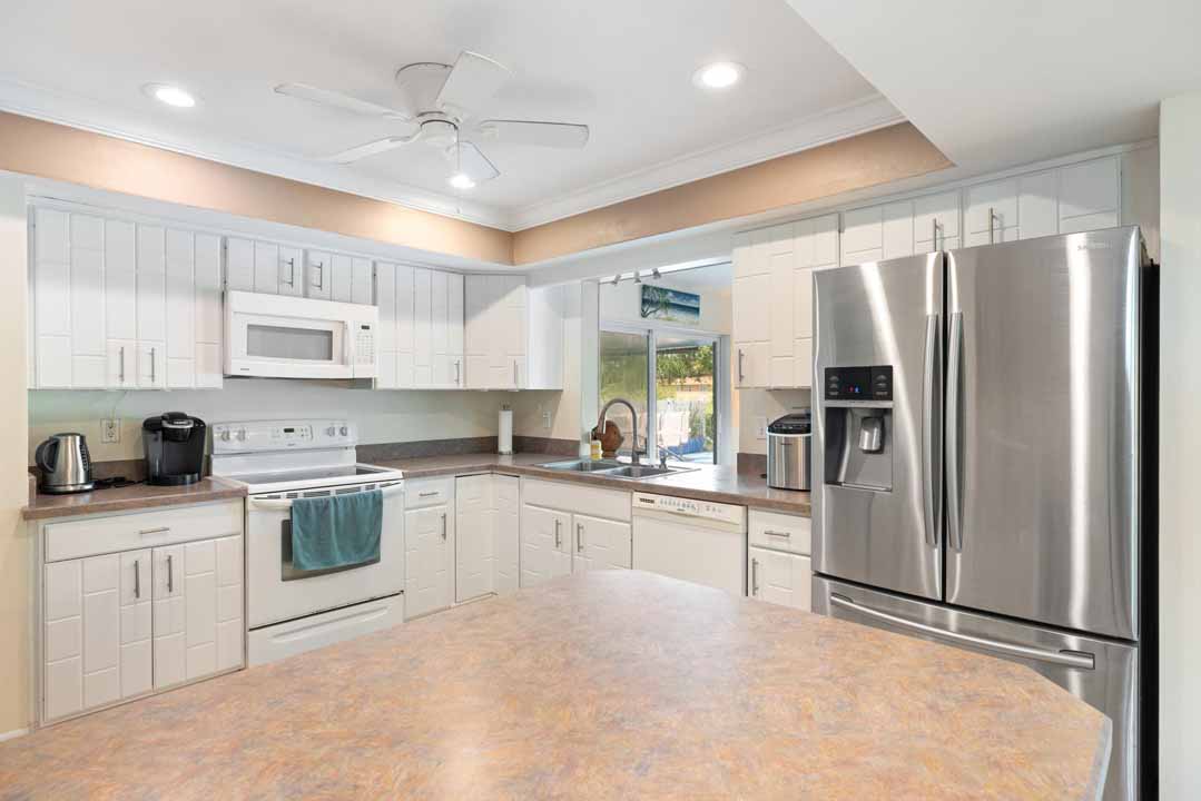 Modern kitchen interior with white cabinetry, stainless steel appliances, and a view of the Rotonda backyard through a window above the sink.