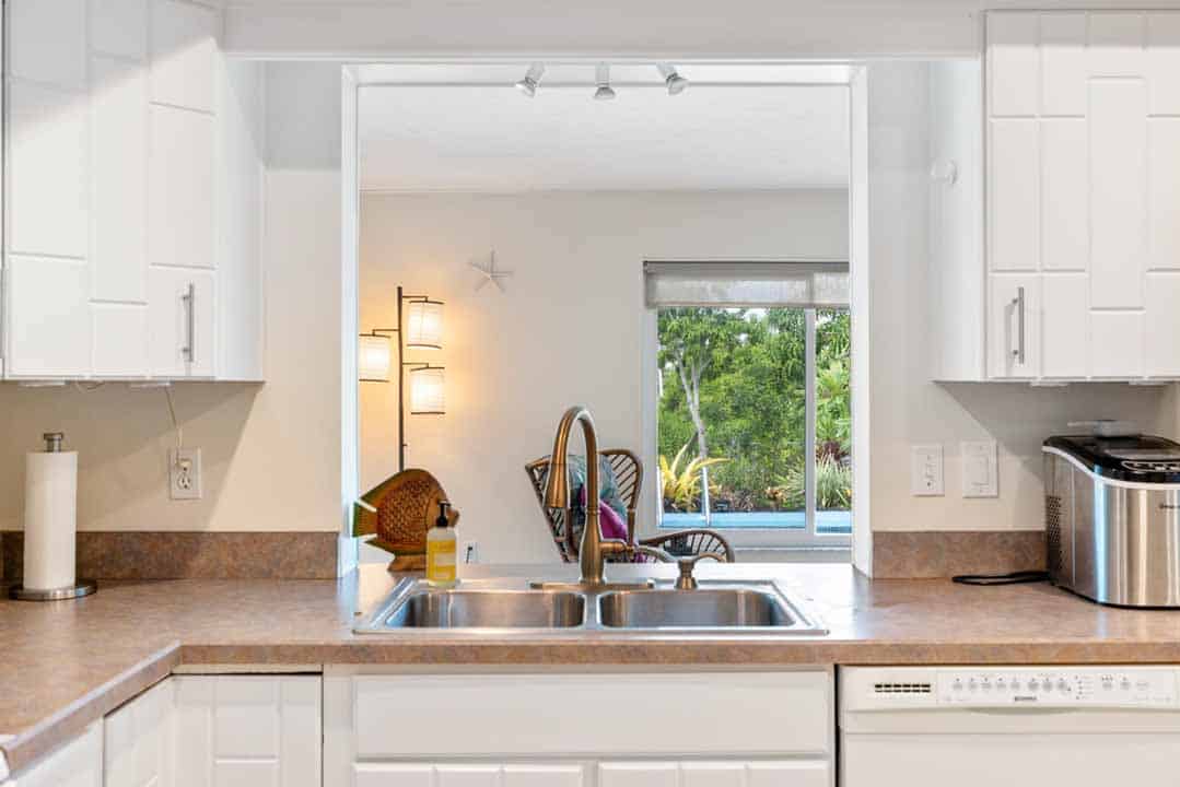 Modern kitchen with white cabinets, granite countertops, and a view of a garden through a Rotonda-style pass-through window.