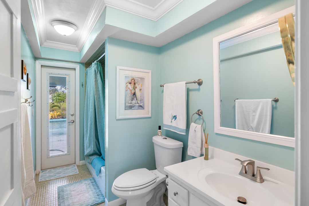 Modern bathroom with teal walls featuring a white vanity, toilet, and framed artwork, leading to a shower curtain and a visible architectural view.