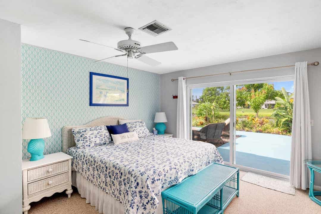 Interior of a bright bedroom with a patterned blue and white bedspread, sliding doors leading to a garden, and Rotonda-inspired decor.