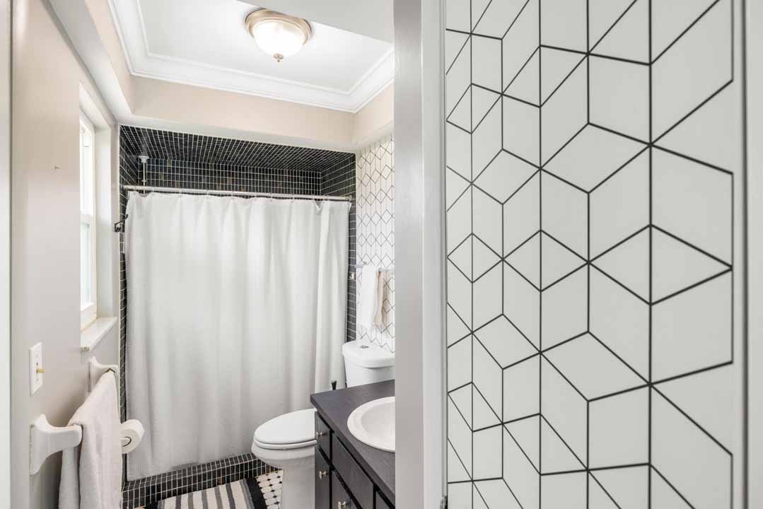 Modern bathroom with geometric patterned tiles, black and white interior, featuring a Rotonda shower stall with a white curtain, a toilet, and a vanity sink.