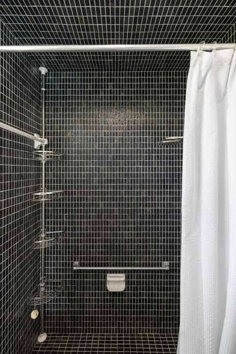 Modern bathroom with a small, tiled shower enclosed by a white Rotonda curtain, featuring a metallic showerhead and shelf.