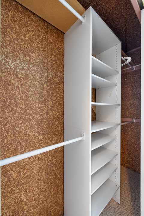 Empty white shelving unit inside a small Rotonda closet with cork wall lining and a single metal hanging rod.