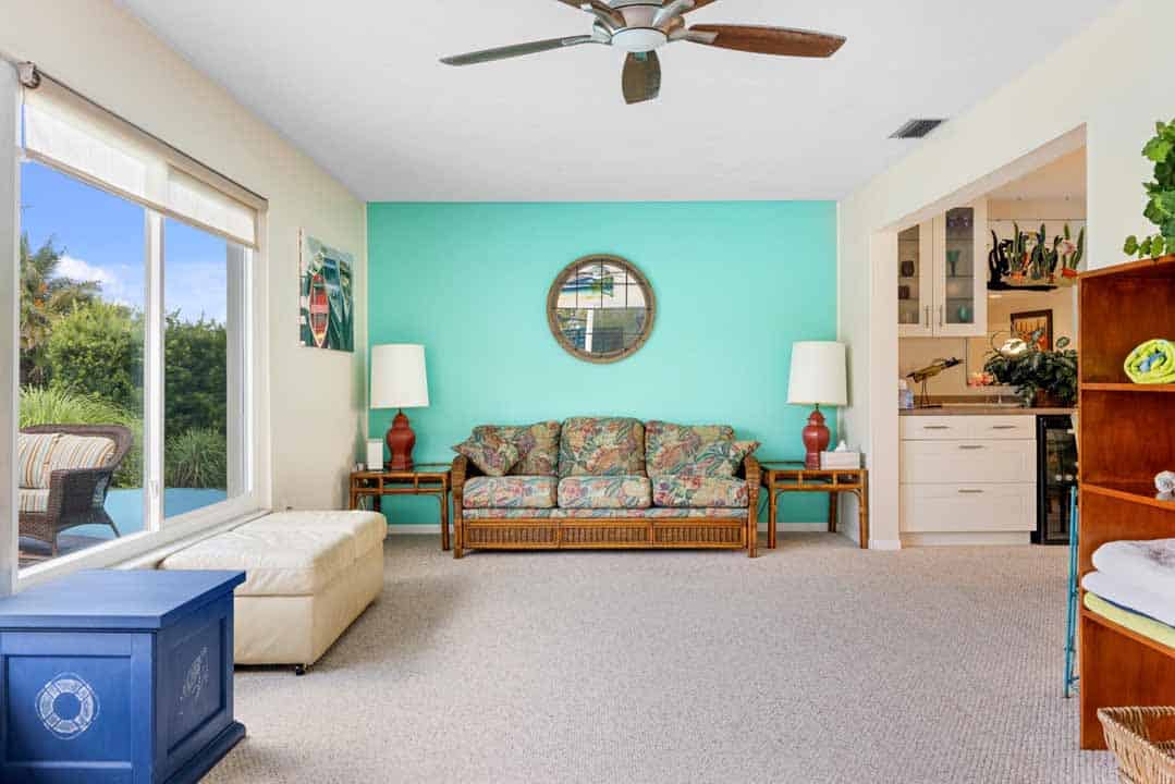 Bright living room with tropical decor, featuring a floral sofa, two lamps, and a round window on a teal wall in Rotonda, Florida.