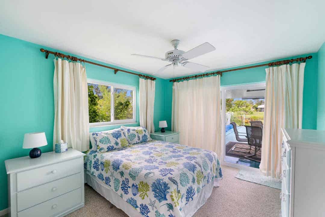 Bright bedroom with turquoise walls, a floral bedspread, and glass doors leading to a patio with a pool view in Rotonda.