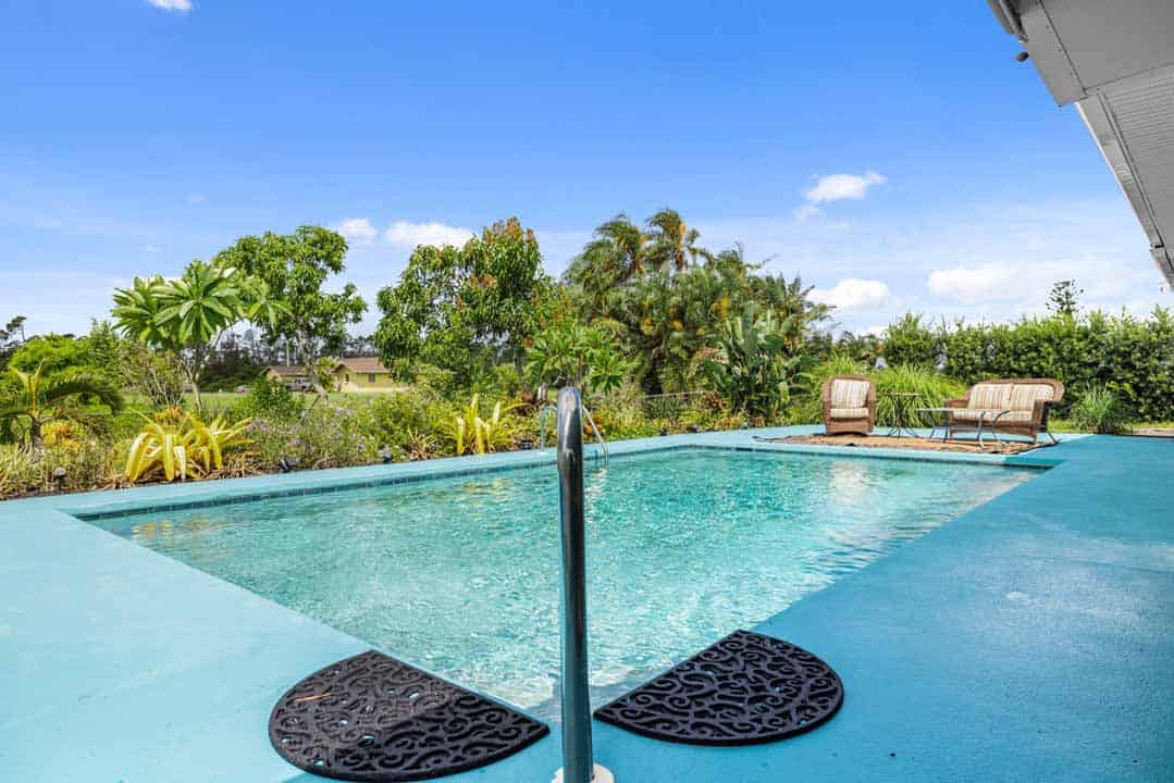 Swimming pool with lounge chairs in a Rotonda, surrounded by lush tropical vegetation under a clear blue sky.