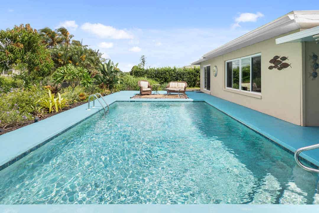 A well-maintained backyard swimming pool in Rotonda beside a single-story house, with sun loungers on the deck and lush greenery surrounding the area.
