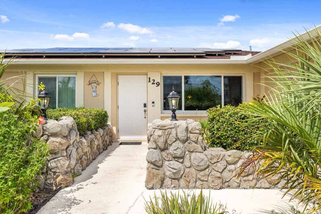 Modern single-story house in Rotonda, Florida, with solar panels on the roof, a stone-lined path leading to the front door, surrounded by lush greenery under a clear blue sky.