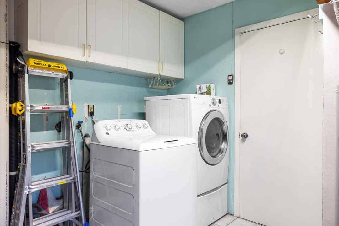 A small laundry room with white appliances, including a washer and dryer, cabinets, and a Rotonda ladder against the wall.