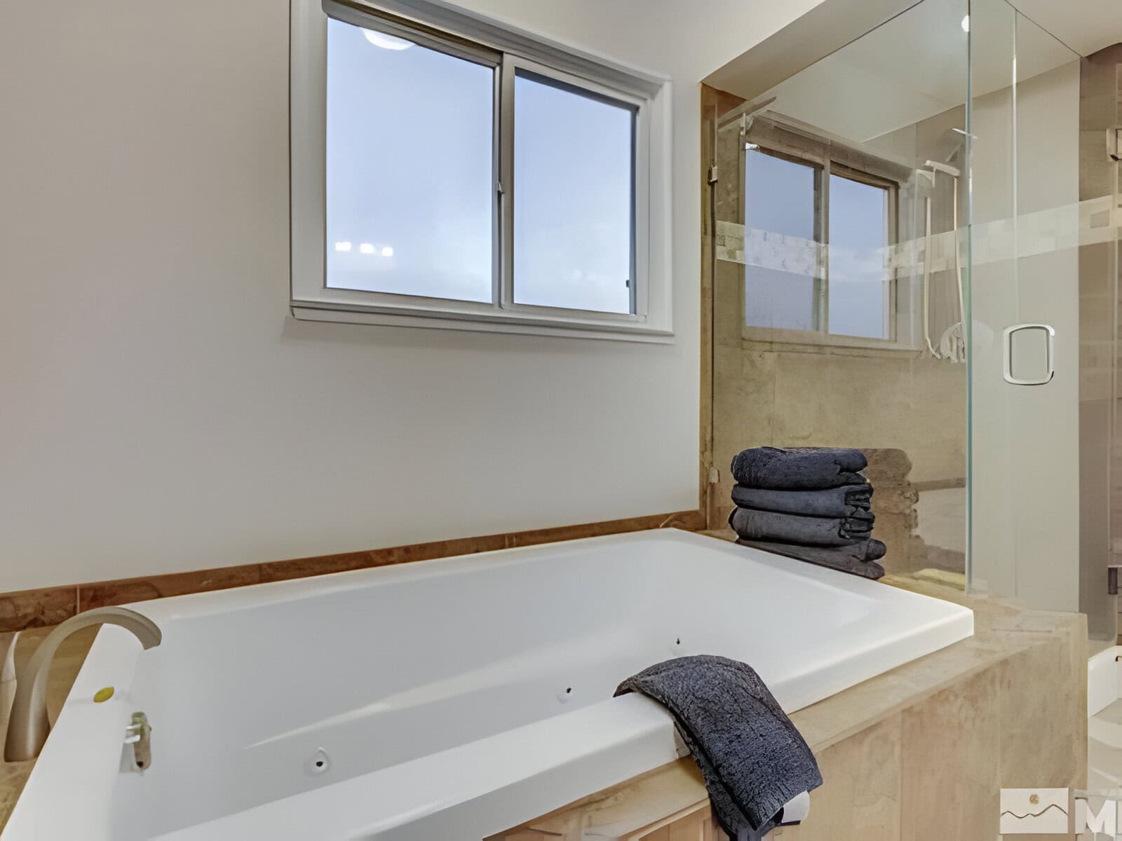 Bathroom featuring a white bathtub, glass shower enclosure, window, and a stack of folded dark towels.