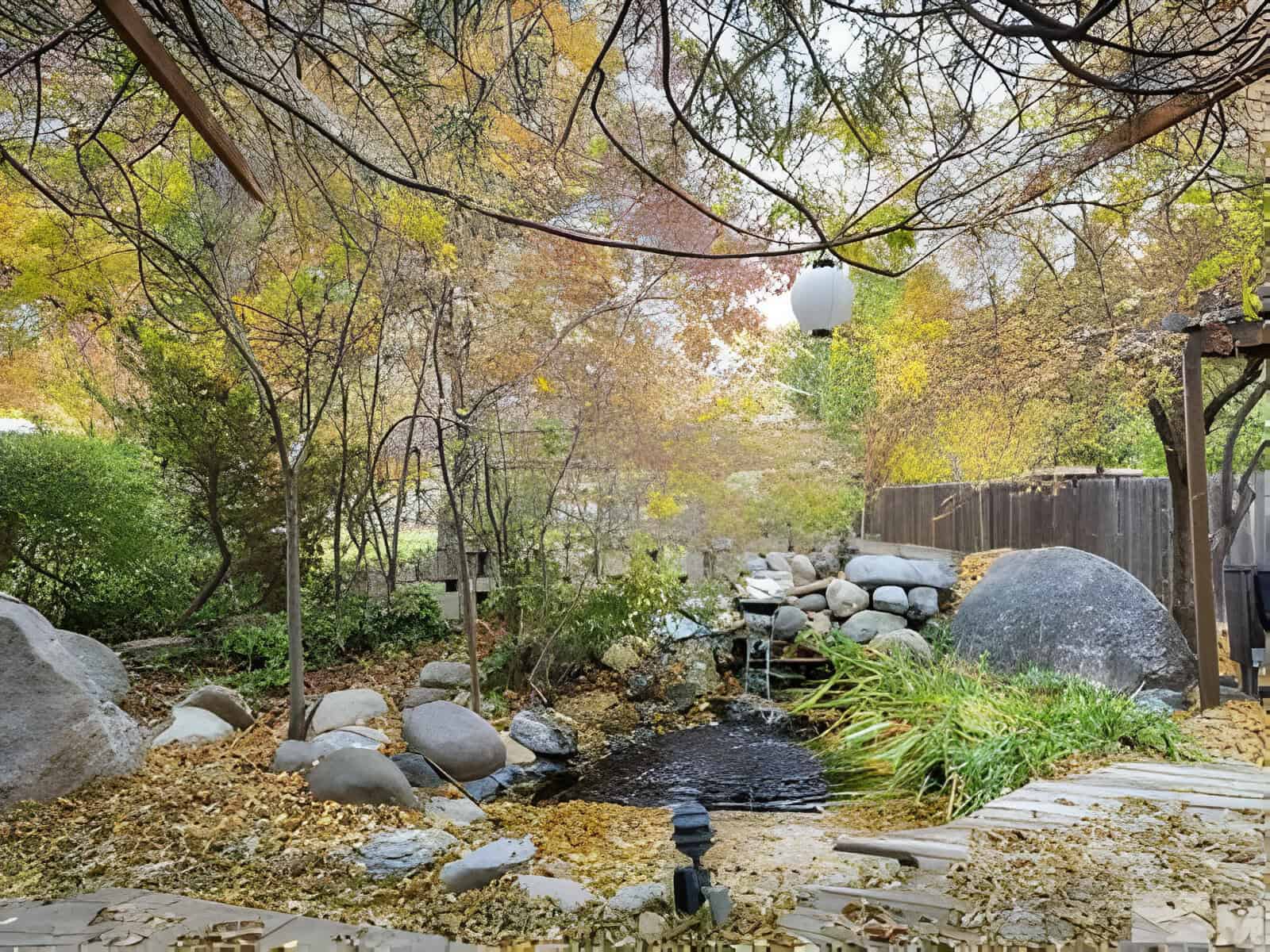Tranquil garden with autumn foliage, pond, rocks, and decorative lantern. Wooden path crosses stream beneath leaf-laden trees.