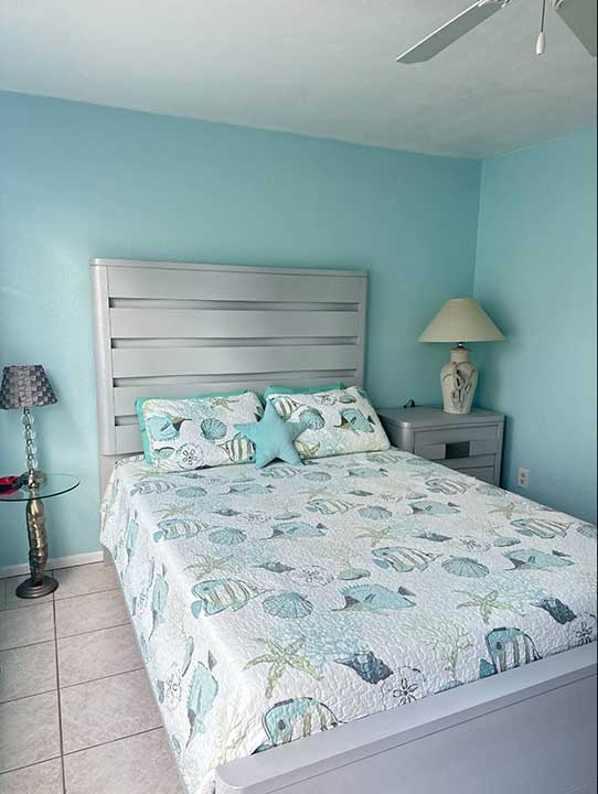 This serene bedroom embraces a light blue theme, highlighted by a sea-themed quilt and matching pillows. Nestled at 4410 Warren Ave, it features two lamps resting on stylish side tables for a perfect touch of elegance and tranquility.